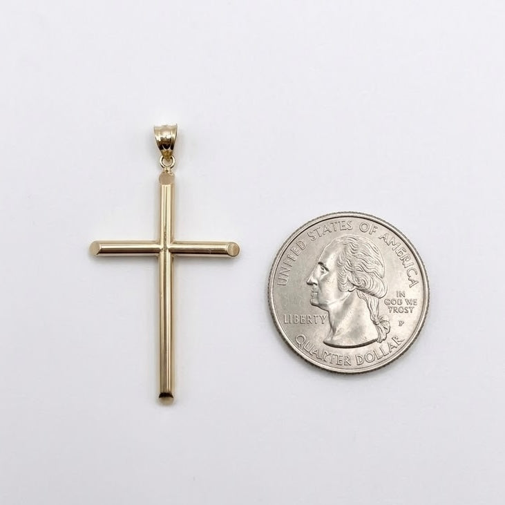 A gold cross pendant displayed next to a US quarter coin for scale, set against a plain white background.