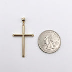 A gold cross pendant displayed next to a US quarter coin for scale, set against a plain white background.