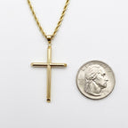 A gold cross pendant necklace on a gold chain, displayed next to a US dime for scale on a plain white background.