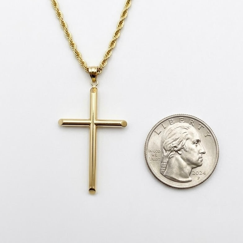 A gold cross pendant necklace on a gold chain, displayed next to a US dime for scale on a plain white background.
