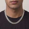 A close-up of a man wearing a thick, polished silver Cuban link chain necklace over a black t-shirt, cropped from the chin down.