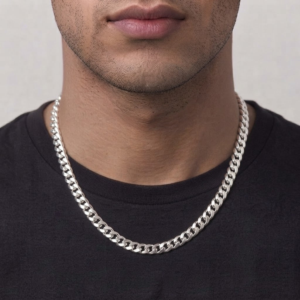 A close-up of a man's neck and lower face wearing a thick, polished silver Cuban link chain necklace over a black t-shirt.