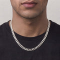 A close-up of a man's neck and lower face wearing a thick, polished silver Cuban link chain necklace over a black t-shirt.