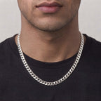 A close-up of a man's neck and lower face wearing a thick, polished silver Cuban link chain necklace over a black t-shirt.