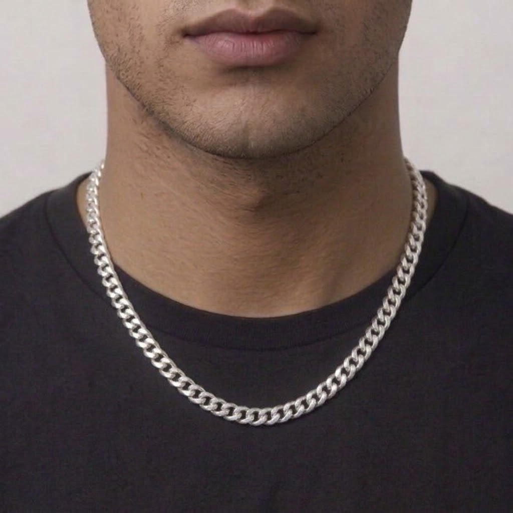 A close-up of a man wearing a thick silver Cuban link chain necklace over a black t-shirt, cropped from the chin down.
